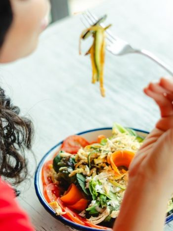 A woman in a red shirt enjoys a fresh salad indoors at a restaurant table.