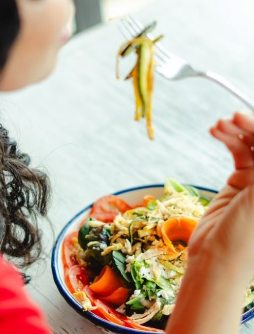 A woman in a red shirt enjoys a fresh salad indoors at a restaurant table.